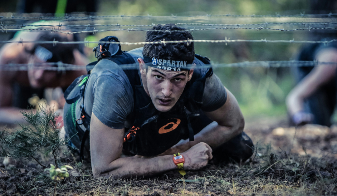 An athlete crawling under barbed wire in a spartan-type race event.