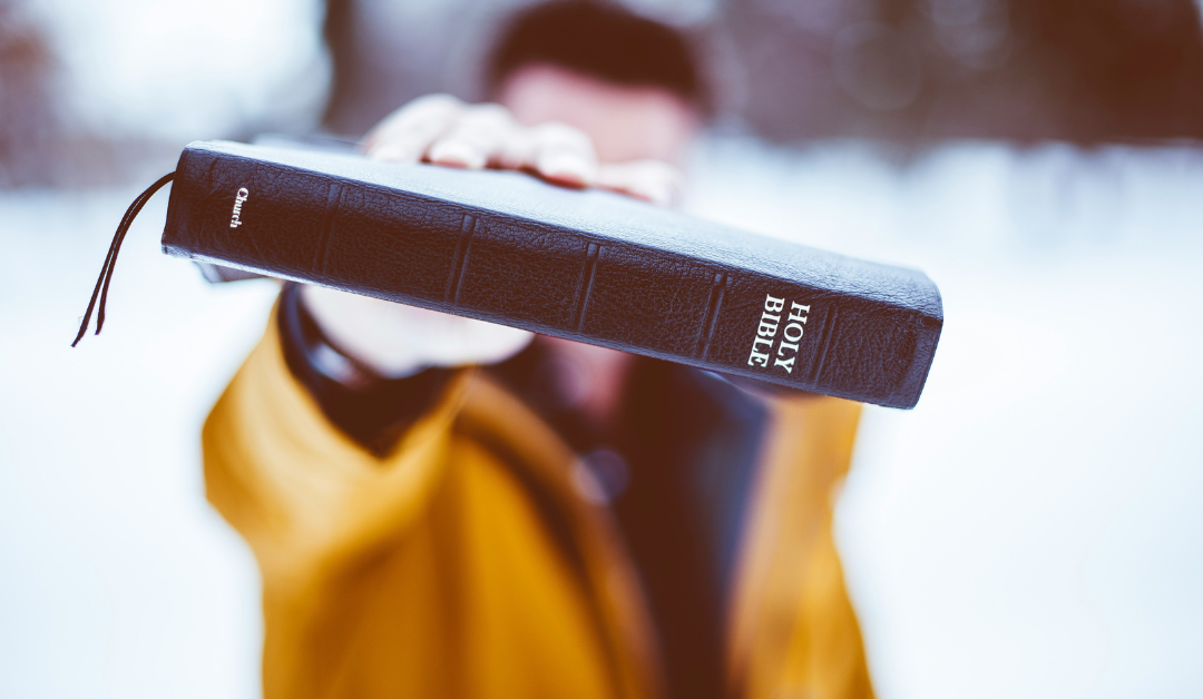 A man holding a Bible toward the viewer